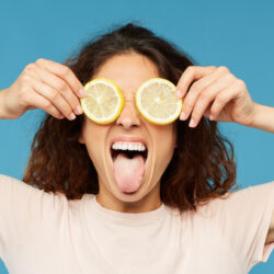 Young brunette healthy woman holding two lemon slices by her eyes